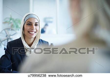 Stock Photo - Over shoulder view of young businesswoman chatting to colleague in office. Fotosearch