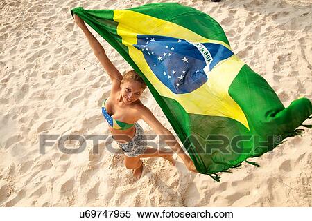 Stock Photography - "Overhead portrait of young woman holding Brazilian flag whilst dancing, Ipanema beach, Rio De Janeiro, Brazil". Fotosearch