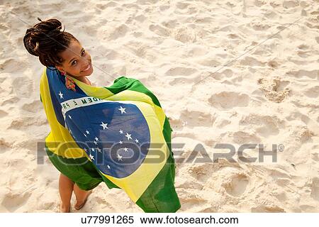 Stock Photography - "Overhead portrait of young woman wrapped in Brazilian flag, Ipanema beach, Rio De Janeiro, Brazil". Fotosearch