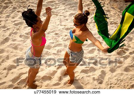 Stock Photo - "Overhead view of two young women holding Brazilian flag whilst dancing, Ipanema beach, Rio De Janeiro, Brazil". Fotosearch