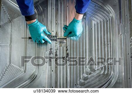 Stock Photo - "Overhead view of worker finishing metal mould in plastics factory, close up". Fotosearch