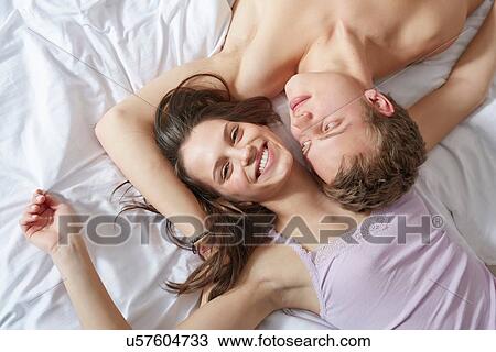 Stock Image - Overhead view of young couple lying on bed. Fotosearch