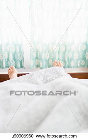 Stock Image - Pair of feet sticking out under duvet. Fotosearch