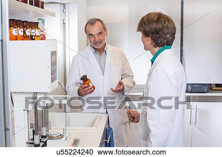 Stock Image - Pharmacist advising trainee on medicine in pharmacy. Fotosearch