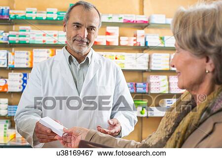 Stock Photo - Pharmacist handing medicine to senior woman in pharmacy. Fotosearch