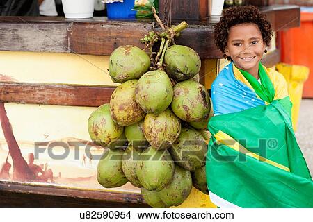 Picture - "Portrait of boy wrapped in Brazilian flag next to bunch of coconuts on Ipanema beach, Rio De Janeiro, Brazil". Fotosearch