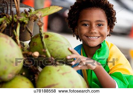 Stock Photo - "Portrait of boy wrapped in Brazilian flag selecting coconut on Ipanema beach, Rio De Janeiro, Brazil". Fotosearch