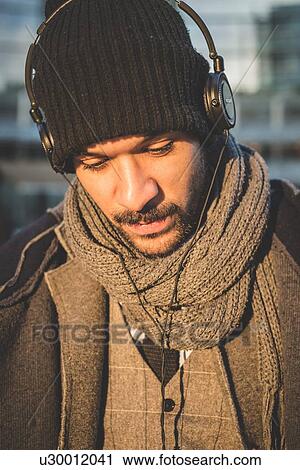 Stock Image - Portrait of businessman looking down and listening to headphones. Fotosearch