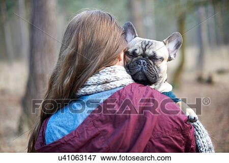 Stock Photo - Portrait of cute dog being carried through forest by young woman. Fotosearch