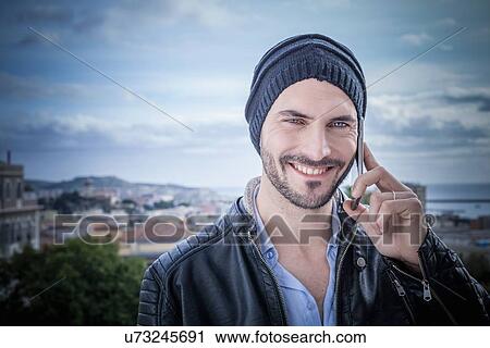 Stock Image - "Portrait of man on rooftop talking on smartphones, Cagliari, Sardinia, Italy". Fotosearch