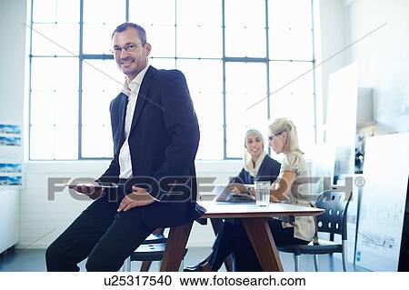 Portrait of mature businessman sitting on office desk View Large Photo Image Stock Image - Portrait of mature businessman sitting on office desk. Fotosearch