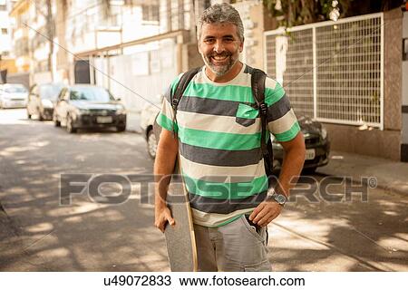 Stock Image - "Portrait of mature man carrying skateboard, Rio De Janeiro, Brazil". Fotosearch