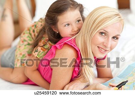 Stock Image - "Portrait of mother and daughter, lying on bed". Fotosearch