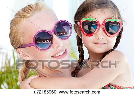 Stock Image - "Portrait of mother and daughter, wearing sunglasses, close-up". Fotosearch