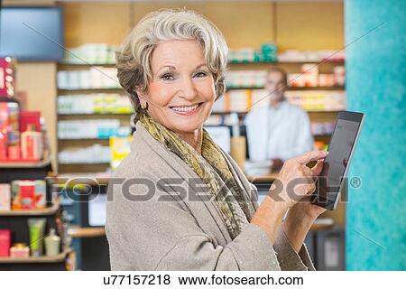 Stock Photo - Portrait of senior woman using digital tablet to check medicine online in pharmacy. Fotosearch
