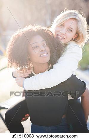 Portrait of two female friends giving piggy backs in park View Large Photo Image Stock Photo - Portrait of two female friends giving piggy backs in park. Fotosearch