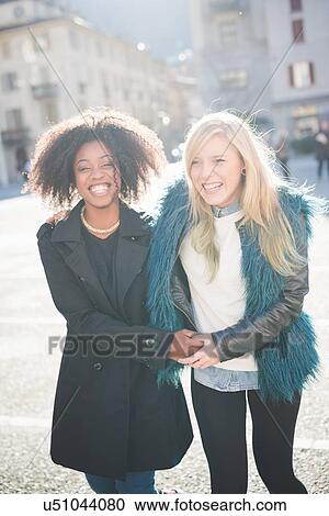 Stock Image - Portrait of two female friends laughing in town square. Fotosearch