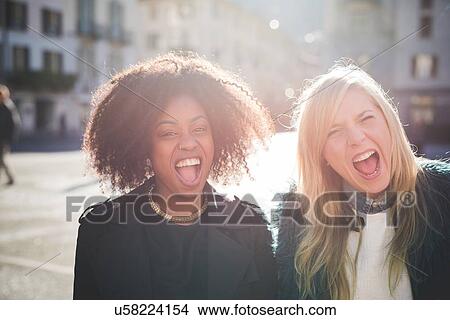 Picture - Portrait of two laughing female friends in town square. Fotosearch