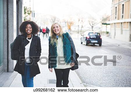 Stock Image - "Portrait of two young female friends strolling along street, Como, Italy". Fotosearch