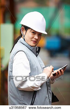 Stock Photo - "Portrait of worker using smartphone at shipyard, GoSeong-gun, South Korea". Fotosearch