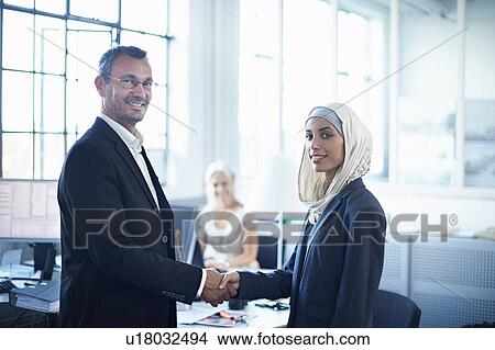 Portrait of young businesswoman shaking hands with businessman in office View Large Photo Image Picture - Portrait of young businesswoman shaking hands with businessman in office. Fotosearch