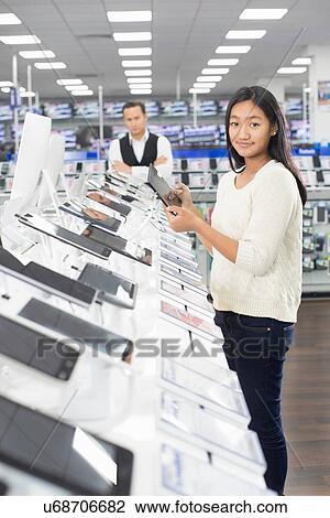 Portrait of young female shopper browsing digital tablets in electronics store View Large Photo Image Stock Image - Portrait of young female shopper browsing digital tablets in electronics store. Fotosearch