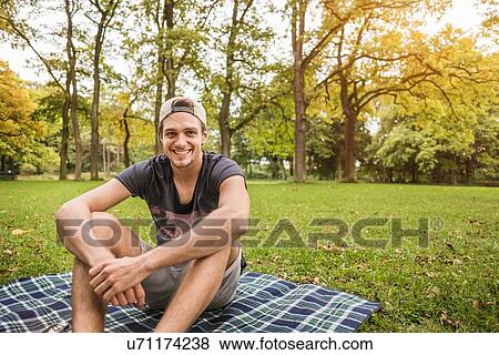 Portrait of young man sitting on picnic blanket in park View Large Photo Image Stock Photo - Portrait of young man sitting on picnic blanket in park. Fotosearch