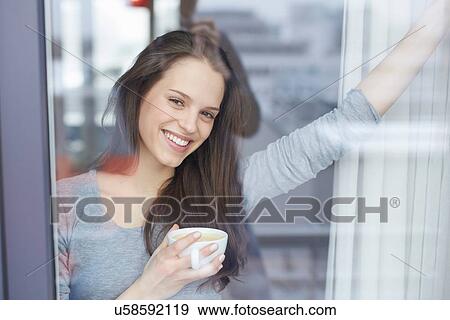 Portrait of young woman at apartment window drinking coffee View Large Photo Image Stock Photo - Portrait of young woman at apartment window drinking coffee. Fotosearch