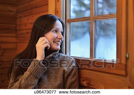 Stock Photo - "Portrait of young woman chatting on smartphone and looking out of window, Posio, Lapland, Finland". Fotosearch