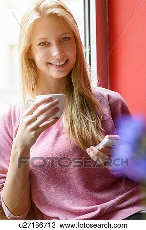 Portrait of young woman drinking coffee whilst using smartphone in cafe View Large Photo Image Stock Image - Portrait of young woman drinking coffee whilst using smartphone in cafe. Fotosearch