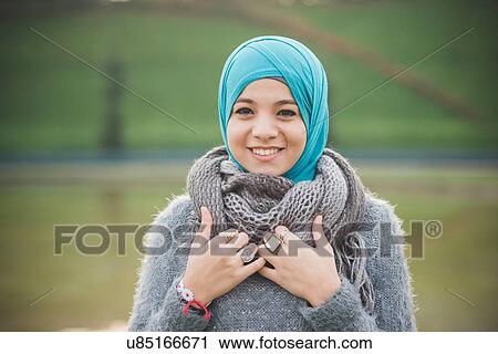 Stock Image - Portrait of young woman in park wearing turquoise hijab. Fotosearch