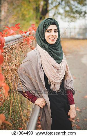 Stock Photo - Portrait of young woman leaning against railing on park path. Fotosearch
