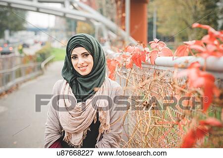 Portrait of young woman leaning against fence on park path View Large Photo Image Stock Photo - Portrait of young woman leaning against fence on park path. Fotosearch