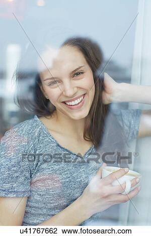 Portrait of young woman looking out of apartment window drinking coffee View Large Photo Image Stock Image - Portrait of young woman looking out of apartment window drinking coffee. Fotosearch