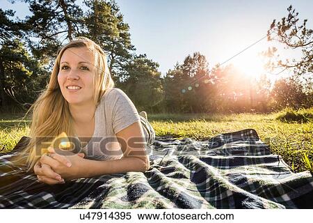 Stock Photography - Portrait of young woman lying on picnic blanket in park. Fotosearch