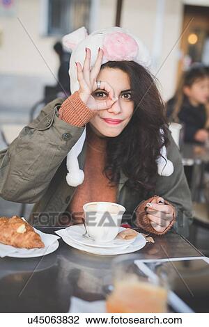 Stock Image - Portrait of young woman making ok hand gesture at sidewalk cafe. Fotosearch