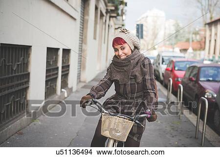 Picture - "Portrait of young woman riding bicycle, wearing winter clothes". Fotosearch