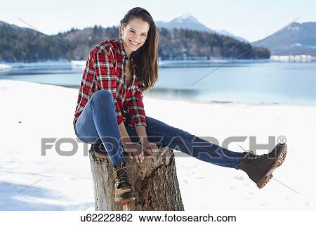 "Portrait of young woman sitting on tree stump at snow covered lakeside, German Alps, Germany" View Large Photo Image Stock Image - "Portrait of young woman sitting on tree stump at snow covered lakeside, German Alps, Germany". Fotosearch