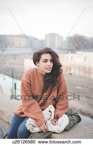 Portrait of young woman sitting on wall looking away View Large Photo Image Stock Image - Portrait of young woman sitting on wall looking away. Fotosearch