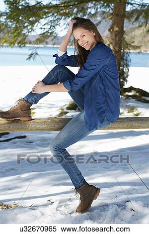 Stock Photography - "Portrait of young woman standing on fence at snow covered lakeside, German Alps, Germany". Fotosearch