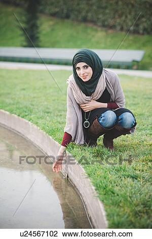 Portrait of young woman wearing hijab crouching at park lake View Large Photo Image Stock Image - Portrait of young woman wearing hijab crouching at park lake. Fotosearch