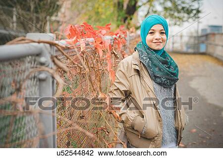 Stock Image - Portrait of young woman with hands in pocket on park path. Fotosearch