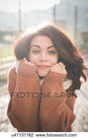 Stock Image - Portrait of young woman with hands on chin in park. Fotosearch