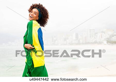Stock Image - "Portrait of young woman wrapped in Brazilian flag on Ipanema beach, Rio De Janeiro, Brazil". Fotosearch