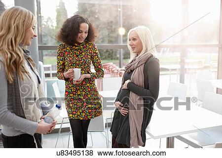 Stock Photo - Pregnant businesswoman chatting to female colleagues in office. Fotosearch