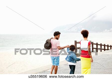 Stock Photograph - "Rear view of couple and son strolling hand in hand, Ipanema beach, Rio De Janeiro, Brazil". Fotosearch
