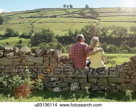 Rear view of farming couple looking out from dry stone wall over field View Large Photo Image Picture - Rear view of farming couple looking out from dry stone wall over field. Fotosearch