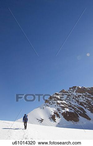 Stock Image - "Rear view of man hiking across snow covered landscape, Jungfrauchjoch, Grindelwald, Switzerland". Fotosearch