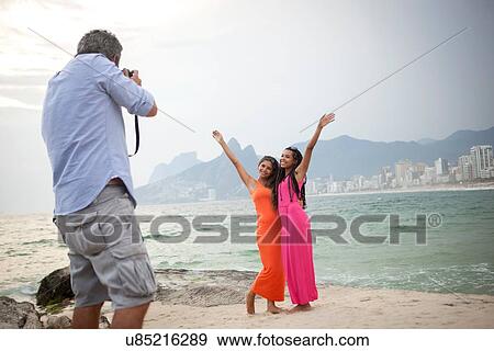 Stock Photo - "Rear view of man photographing two young women on Ipanema beach, Rio De Janeiro, Brazil". Fotosearch