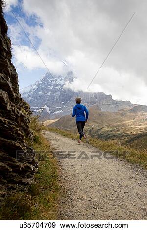 Stock Photo - "Rear view of man running along dirt track toward mount Eiger, Grindelwald, Switzerland". Fotosearch